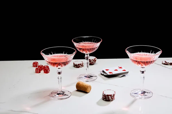 Glasses of cocktail, dice, cork, casino tokens and playing cards on white surface isolated on black — Stock Photo