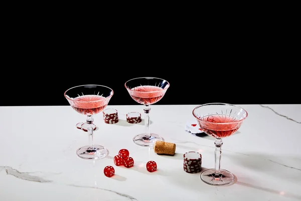 Vista ad alto angolo di bicchieri di cocktail, dadi, sughero, chip da casinò e mazzo di carte su superficie bianca isolata su nero — Foto stock