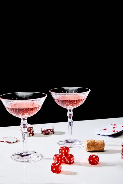 Glasses of cocktail, dice, cork, casino chips and pack of cards on white surface isolated on black — Stock Photo