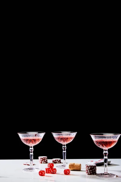 Bicchieri di cocktail, dadi, sughero, chips di casinò e mazzo di carte sulla superficie isolata su nero — Foto stock