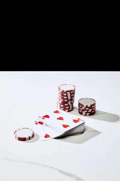 Hochwinkelansicht von Casino-Chips in der Nähe von Kartenstapeln auf weißer Oberfläche isoliert auf schwarzer — Stockfoto