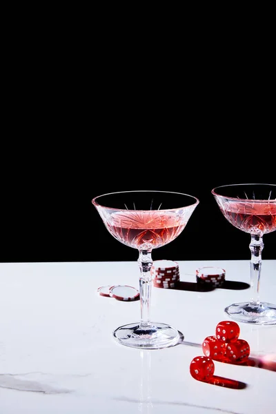 Bicchieri di cocktail, fiches da casinò e dadi su superficie bianca isolati su nero — Foto stock