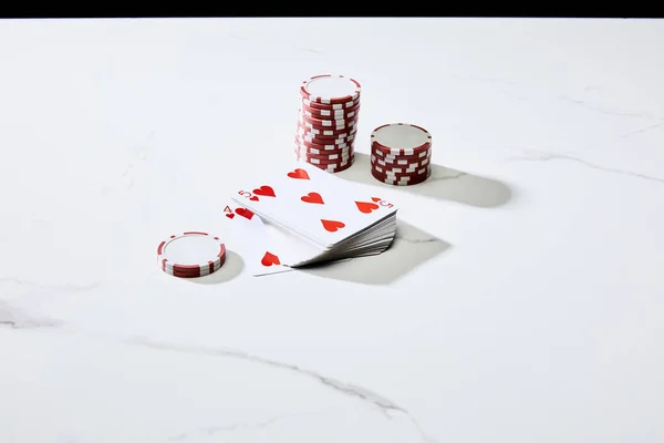 Vista de alto ángulo de fichas de casino con baraja de cartas en la superficie blanca aislado en negro - foto de stock