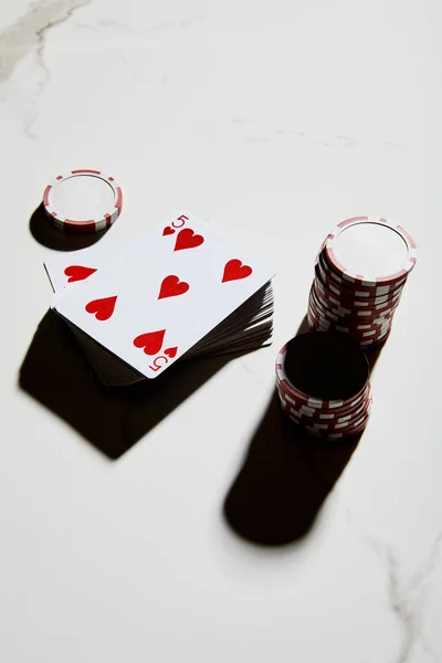 Vista de alto ángulo de fichas de casino con baraja de cartas sobre fondo blanco - foto de stock