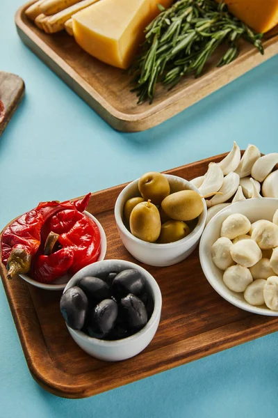 High angle view of bowls with olives, mozzarella and marinated chili peppers with antipasto ingredients on boards on blue — Stock Photo