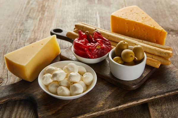 High angle view of bowls with olives, cheese, mozzarella and marinated chili peppers on boards on wooden background — Stock Photo