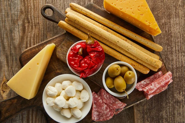 Vista superior de palitos de pan con ingredientes antipasto en tableros sobre fondo de madera - foto de stock