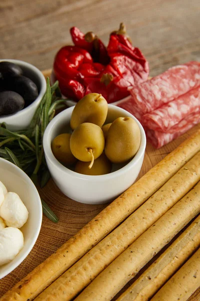 High angle view of breadsticks with antipasto ingredients on round board on wooden background — Stock Photo