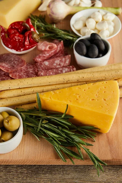 Selective focus of board with cheese, breadsticks, salami slices and antipasto ingredients on wooden background — Stock Photo