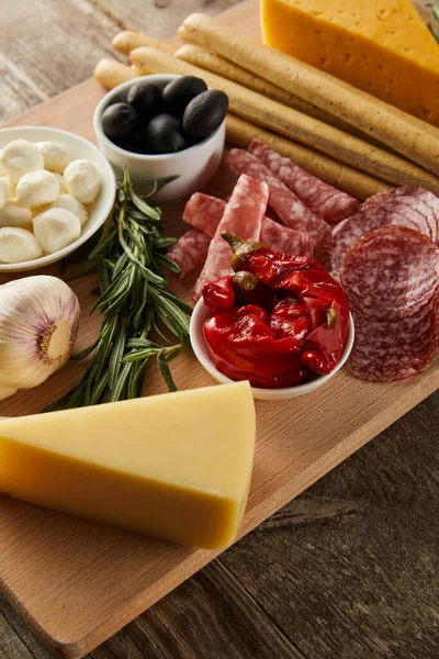 Vista en ángulo alto del tablero con palitos de pan, queso e ingredientes antipasto sobre fondo de madera - foto de stock