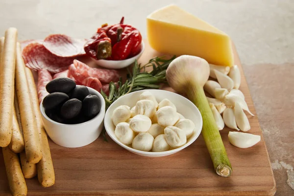 Vista de alto ângulo de bordo com paus de pão, queijo, fatias de salame e ingredientes antipasto em cinza e bege — Fotografia de Stock