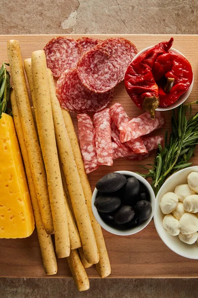 Top view of breadsticks with antipasto ingredients on board on brown — Stock Photo
