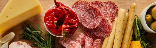 Top view of breadsticks, salami slices, cheese and antipasto ingredients on wooden background, panoramic shot — Stock Photo