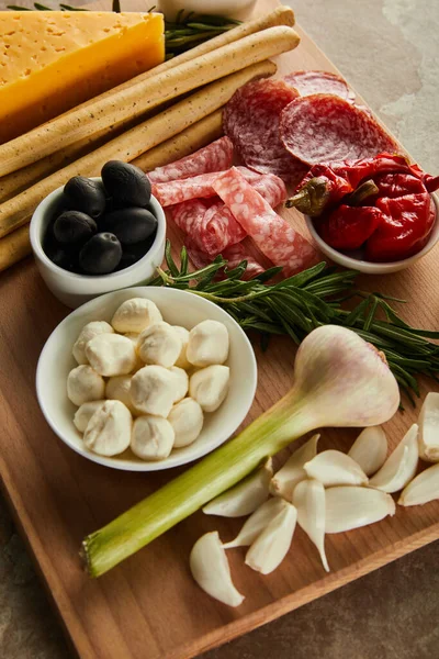 High angle view of board with antipasto ingredients and bowls with mozzarella, olives and marinated chili peppers on brown — Stock Photo