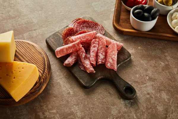 Vista de alto ângulo de tábuas com fatias de salame, tigela com azeitonas e queijo em marrom — Fotografia de Stock