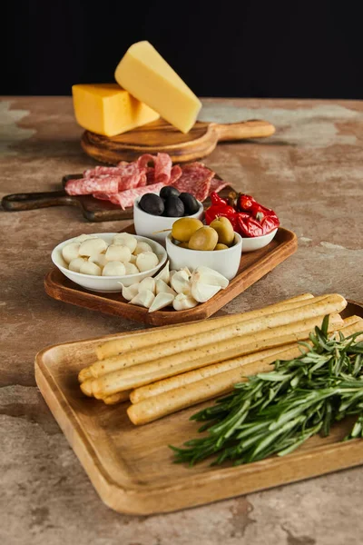 Vista de ángulo alto de los ingredientes antipasto en tableros en superficie marrón aislado en negro - foto de stock