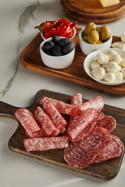 High angle view of boards with salami slices, bowls with olives, mozzarella and marinated chili peppers on white — Stock Photo
