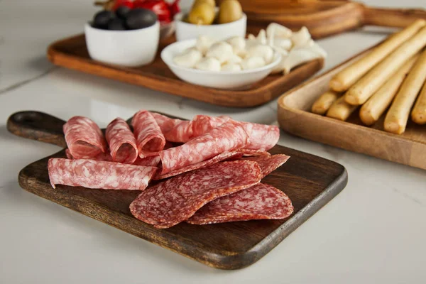 Selective focus of salami slices on board near antipasto ingredients on white — Stock Photo