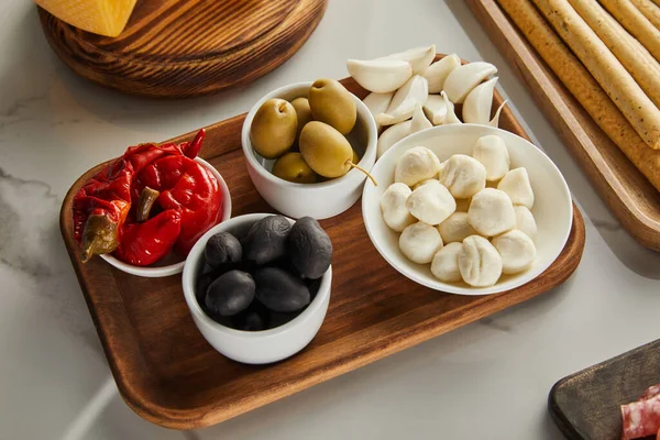 High angle view of boards with breadsticks, garlic and bowls with olives, mozzarella and marinated chili peppers on white — Stock Photo