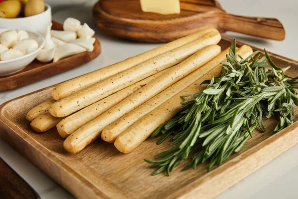 Concentration sélective des planches avec des bâtonnets de pain, du romarin et des ingrédients antipasto sur blanc — Photo de stock