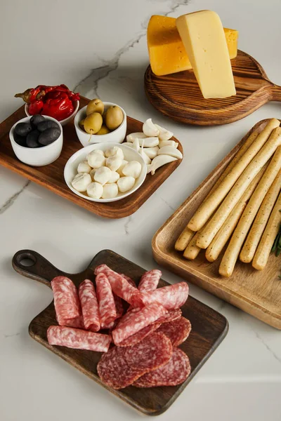 Высокий угол обзора досок с хлебными палочками, ломтиками салями, сыром и антипасто ингредиентами на белом — стоковое фото