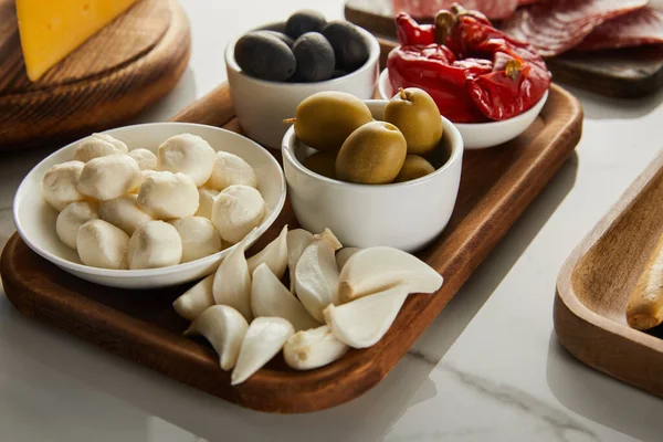 High angle view of boards with garlic and bowls with olives, mozzarella and marinated chili peppers on white — Stock Photo