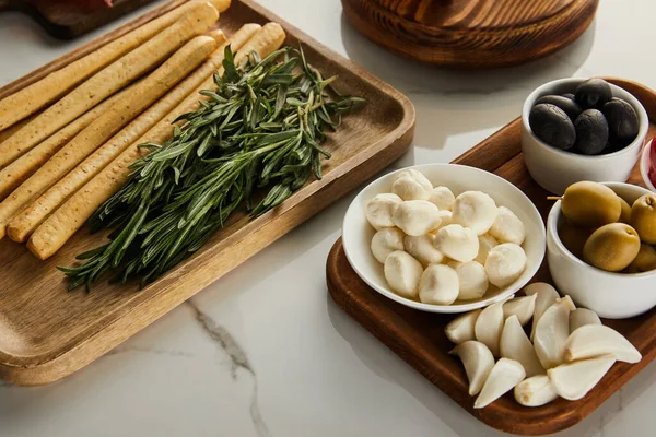 Vue en angle élevé des planches avec des bâtonnets de pain, du romarin et des ingrédients antipasto sur fond blanc — Photo de stock