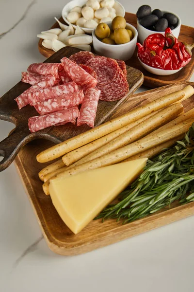 Vue en angle élevé des planches avec tranches de salami, bâtonnets de pain, fromage et ingrédients antipasto sur fond blanc — Photo de stock