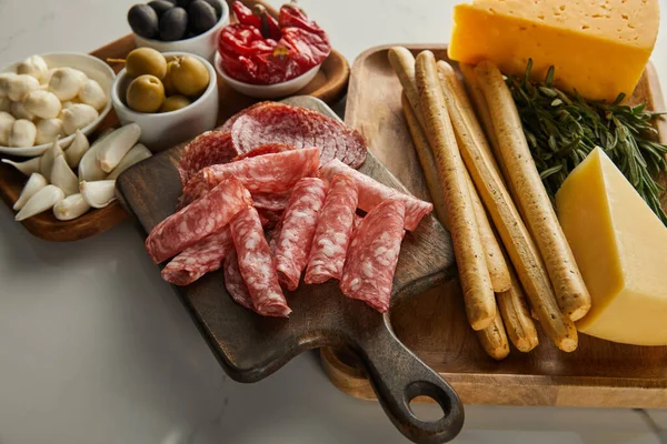 Vue en angle élevé des planches avec des tranches de salami, des bâtonnets de pain, du fromage, de la verdure et des ingrédients antipasto sur blanc — Photo de stock