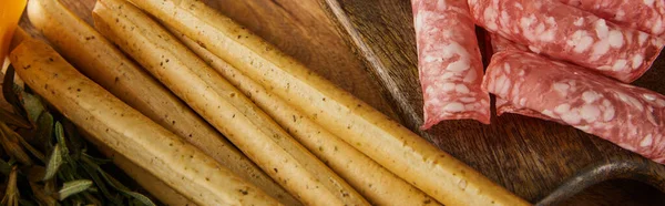 Top view of salami slices and breadsticks on boards, panoramic shot — Stock Photo