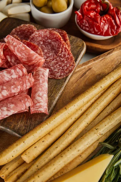 Vista en ángulo alto de rebanadas de salami, palitos de pan e ingredientes antipasto en las tablas — Stock Photo