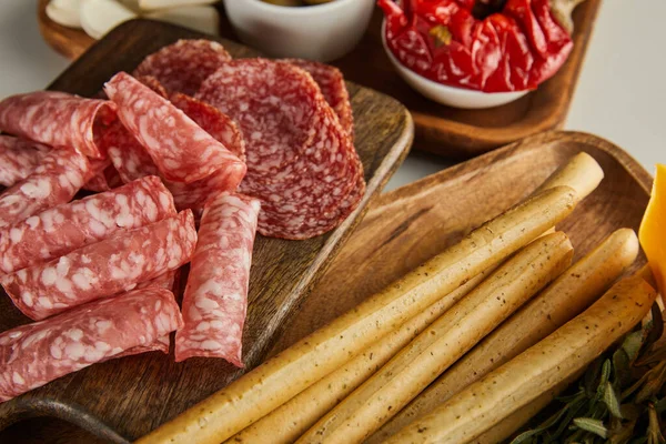 Vista en ángulo alto de rebanadas de salami, palitos de pan e ingredientes antipasto en tablas sobre fondo blanco - foto de stock