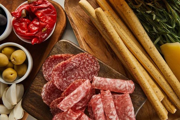 Top view of salami slices and breadsticks with antipasto ingredients on boards on white background — Stock Photo