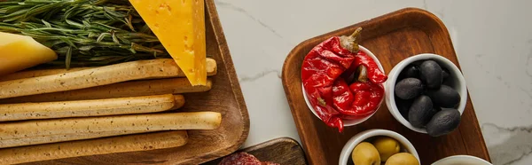 Draufsicht auf Stockbrot, Käse, Grün und Schüsseln mit Antipasto-Zutaten auf weißen Brettern, Panoramaaufnahme — Stockfoto