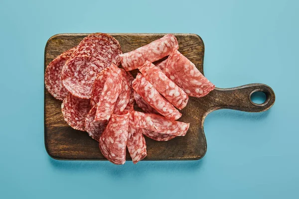 Top view of salami slices on board on blue background — Stock Photo