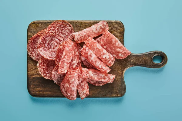 Vue du dessus des tranches de salami à bord sur fond bleu — Photo de stock