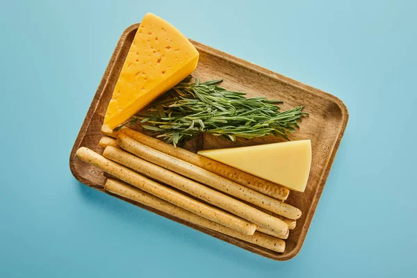 Top view of board with breadsticks, cheese and rosemary on blue — Stock Photo