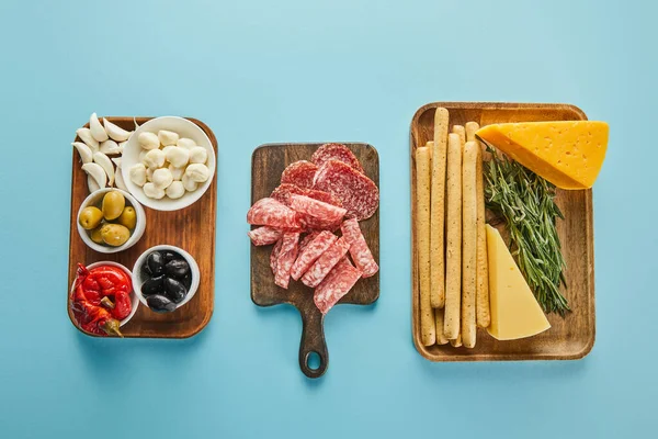 Flat lay with boards with antipasto ingredients on blue background — Stock Photo