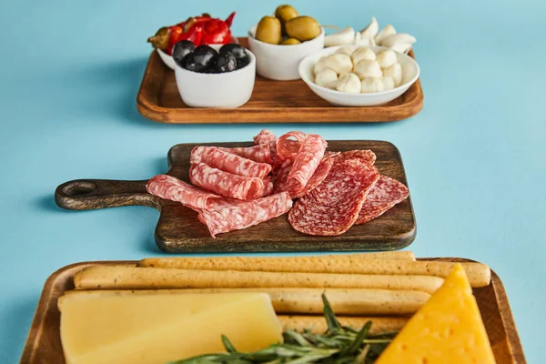 Selective focus of antipasto ingredients on boards on blue background — Stock Photo