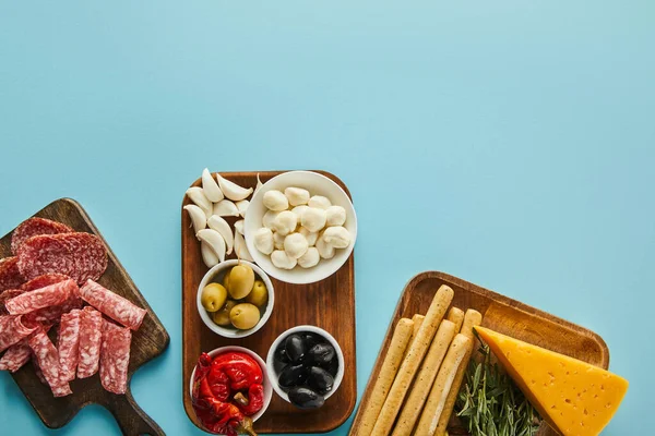 Vue du dessus des planches avec des tranches de salami et des ingrédients antipasto sur fond bleu — Photo de stock