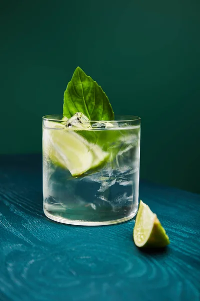 Close up view of old fashioned glass with drink and lime on blue wooden surface isolated on green — Stock Photo