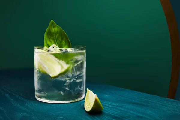 Close up view of old fashioned glass with drink and lime on blue wooden surface isolated on green — Stock Photo