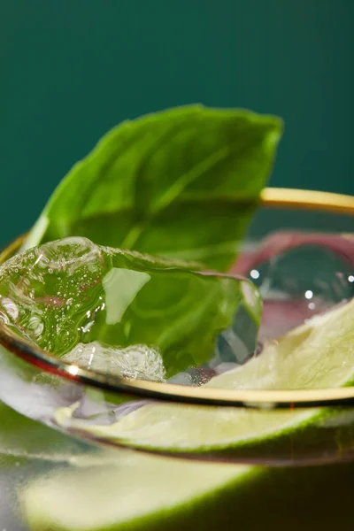 Vista de cerca del vidrio recortado con refrescante mojito, menta y rodaja de lima aislados en verde - foto de stock