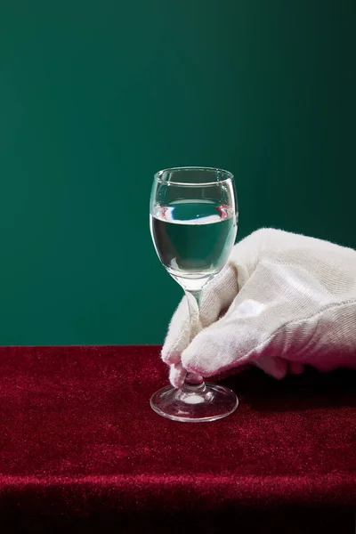 Cropped view of hand in terry glove holding shot glass with liquid isolated on green — Stock Photo