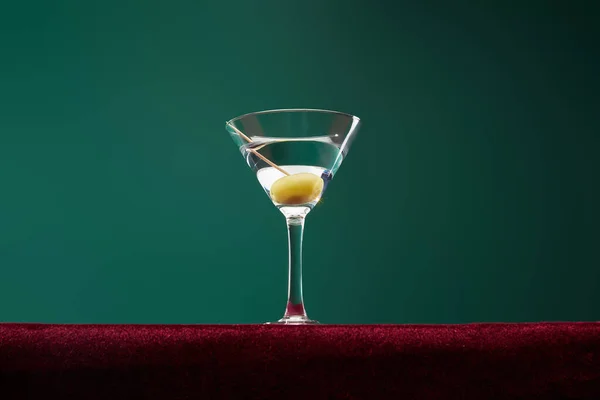 Low angle view of cocktail glass with vermouth and whole olive on toothpick isolated on green — Stock Photo