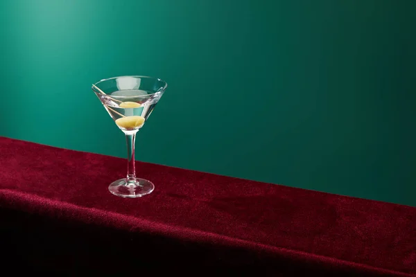 Vue grand angle du verre à cocktail avec vermouth et olive entière sur cure-dent sur surface velours sur fond vert — Photo de stock