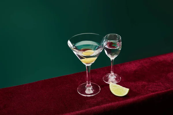 Vue à grand angle du verre à shooter et du verre à cocktail avec vermouth et olive entière sur cure-dent sur surface veloutée isolée sur fond vert — Photo de stock