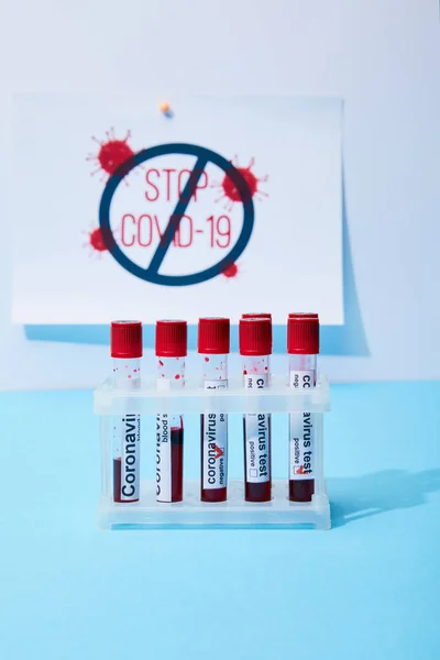 Selective focus of test tubes with coronavirus test samples near paper with stop covid-19 lettering on blue — Stock Photo