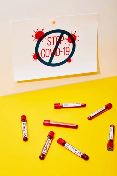 Papel con stop covid-19 cerca de tubos de ensayo con letras de prueba de coronavirus en blanco y amarillo - foto de stock