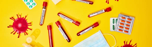 Panoramic shot of test tubes with coronavirus test lettering near medical mask and blister packs with pills on yellow — Stock Photo